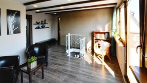 A spacious room with a dark wood floor, a black leather chair, a white baby cradle, a wicker chair, and a bookshelf by a large window. - Large, Comfortable Holiday Villa With a Terrace (Kołobrzeg)