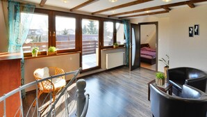 A spacious room with a wooden floor, a bed, a chair, and a balcony with a view. - Large, Comfortable Holiday Villa With a Terrace (Kołobrzeg)