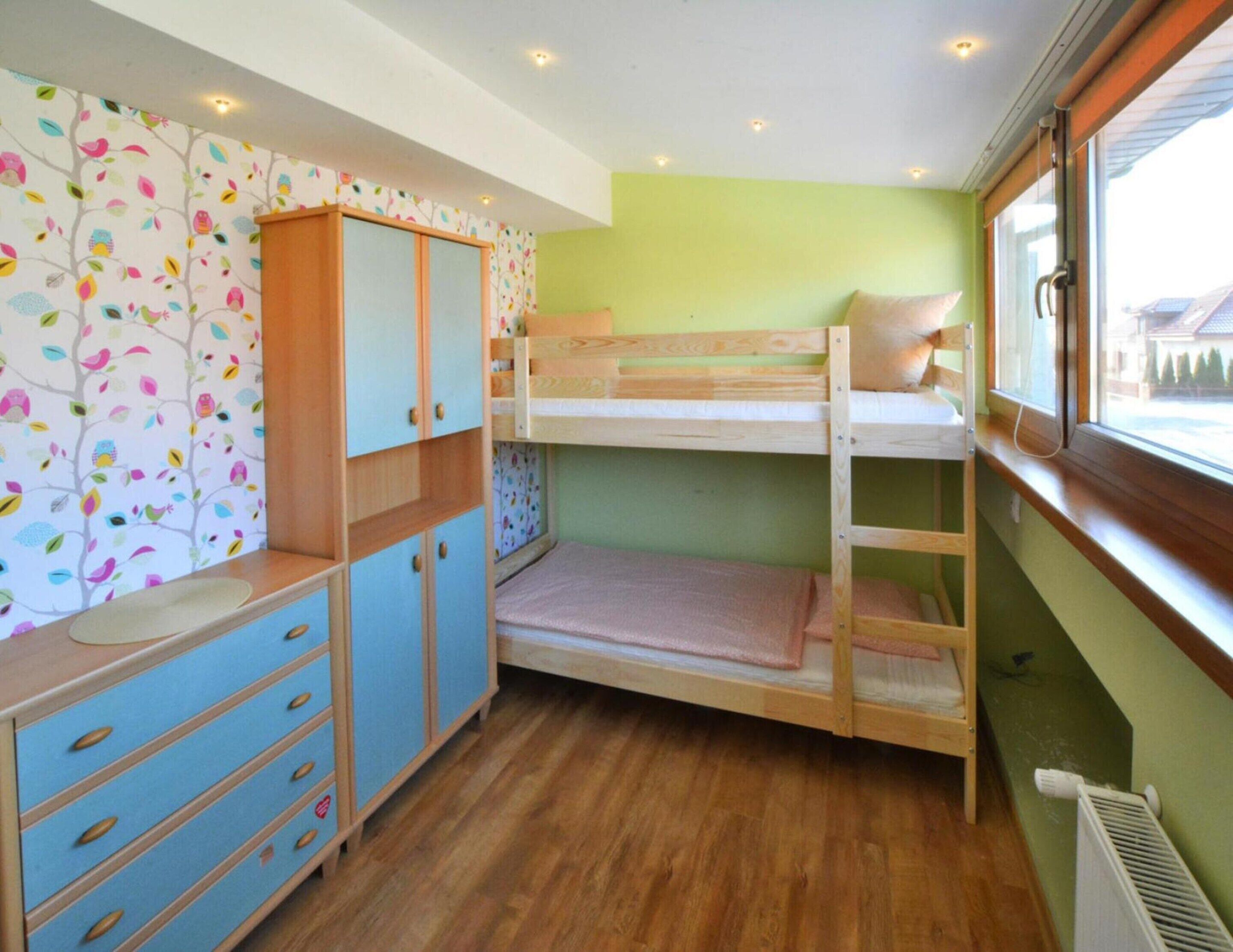 A bunk bed room with a wooden desk and drawers, a radiator, and a window with a view.