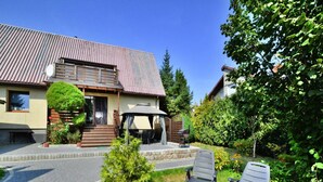 A house with a patio, two lounge chairs, a small garden, and a wooden fence. - Large, Comfortable Holiday Villa With a Terrace (Kołobrzeg)