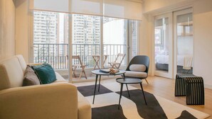 A modern living room with a sofa, a coffee table, and a chair. There is a large window with a view of high-rise buildings. - w* | Duplex Cityview 3BR w/ Balcony in Miraflores (Miraflores)