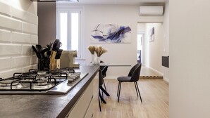 A modern kitchen with a gas stove, a dining area with a glass table, and a contemporary abstract painting on the wall. - Casa Valentina | WiFi, Train Station, Parking (Modena)