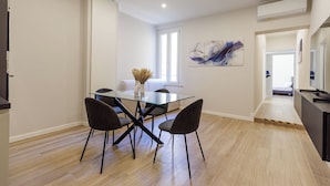 A modern dining area with a glass table and four chairs, a painting on the wall, and an air conditioning unit above. - Casa Valentina | WiFi, Train Station, Parking (Modena)