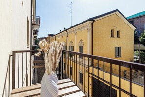 Un balcón con un jarrón blanco de plumas de plumeros, bancos de madera y un edificio amarillo al fondo.