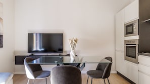 A modern kitchen with a flat-screen TV, a glass dining table, two chairs, and built-in ovens. - Appartamento Chiara| WiFi Stazione Treni Parking (Modena)