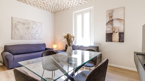 A modern living room with a glass dining table, grey sofa, and artwork on the walls. - Appartamento Chiara| WiFi Stazione Treni Parking (Modena)