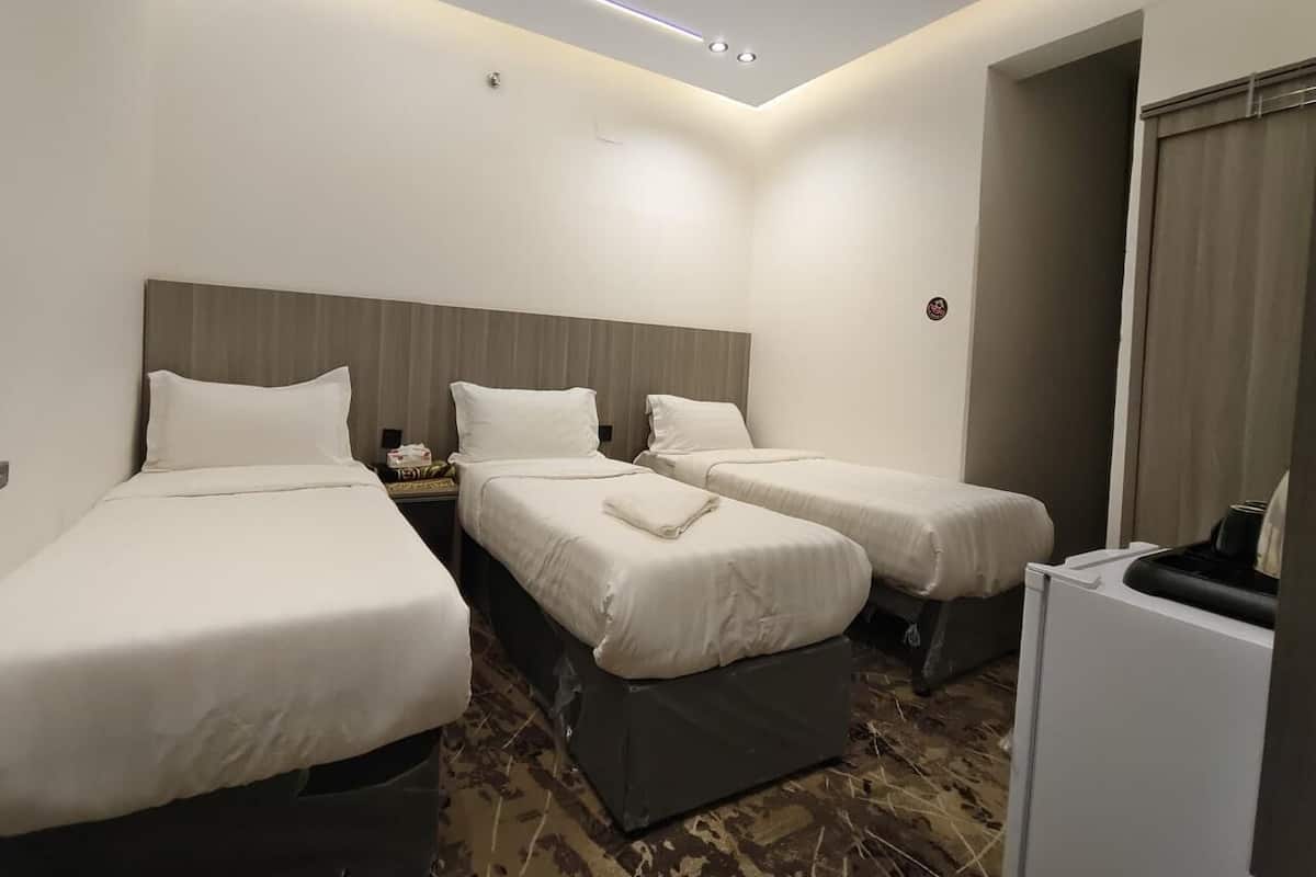 Een hotelkamer met drie eenpersoonsbedden, een klein bureau, een stoel en een witte minibars.