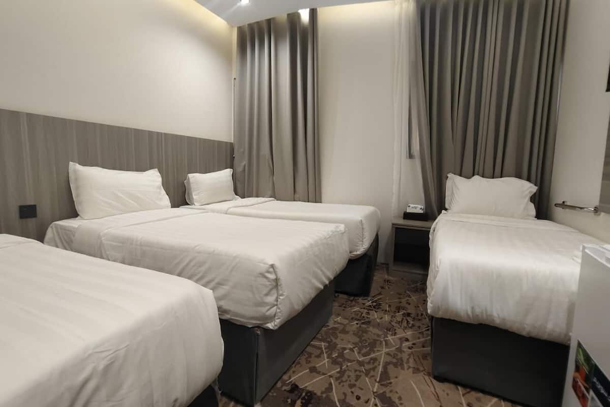 Een hotelkamer met drie eenpersoonsbedden, een klein tafeltje en een televisie.