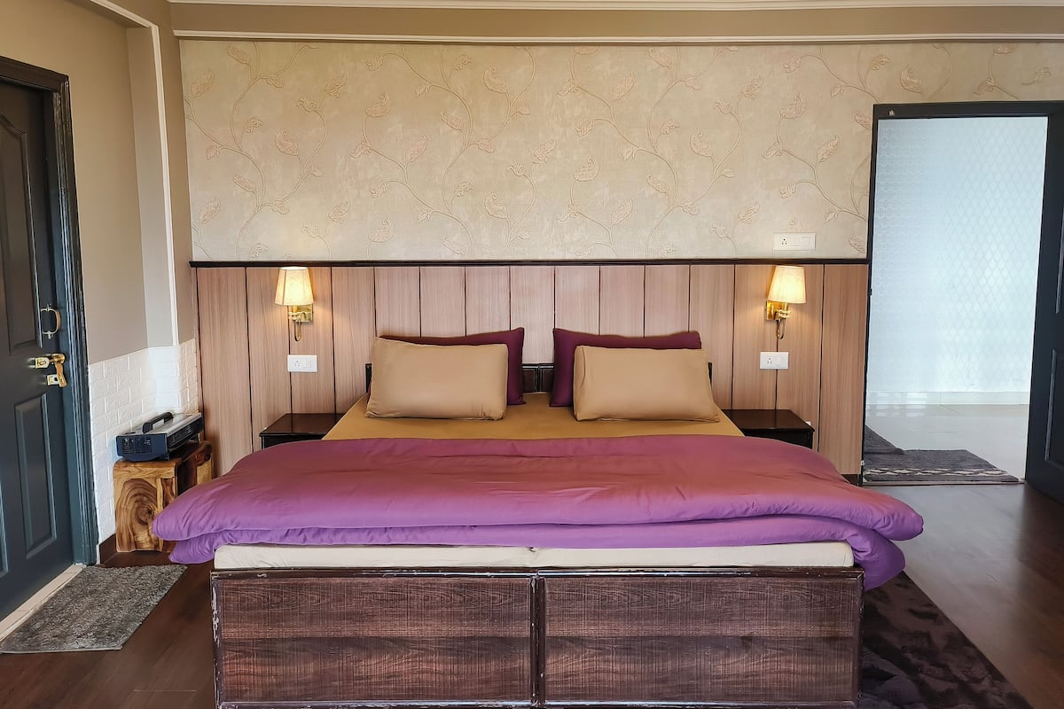Ein Schlafzimmer mit einem hölzernen Kopfteil, zwei Nachttischlampen, einer violetten Bettdecke und einem kleinen Nachttisch mit einem Radio.
