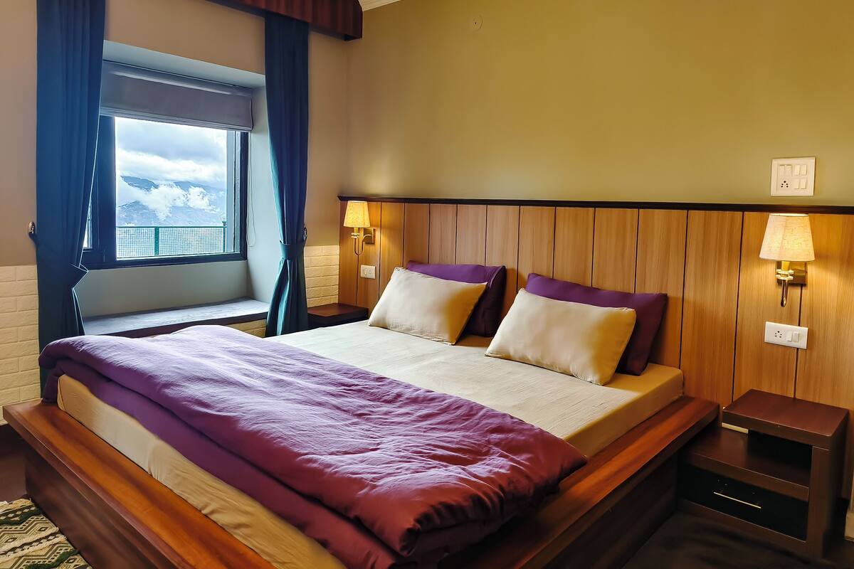Ein Hotelzimmer mit einem großen Bett, zwei Nachttischen, einem Fenster mit Vorhängen und Bergblick.