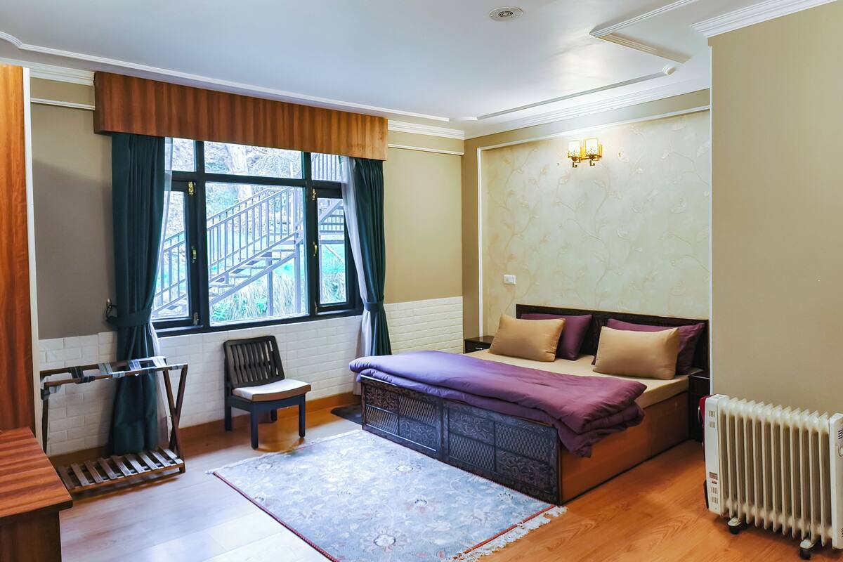 Ein Schlafzimmer mit Bett, Sessel, Heizkörper, Fenster mit Vorhängen und einer Wandleuchte.