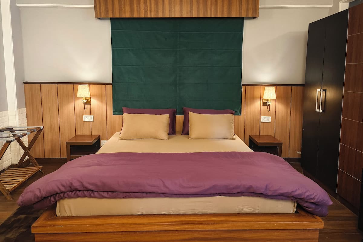 Ein Hotelzimmer mit einem großen Bett, einem hölzernen Kopfteil, zwei Nachttischen mit Lampen, einem Kleiderschrank und einem grünen Vorhang.