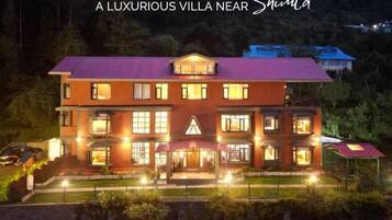 A luxurious villa with multiple floors, large windows, and a well-lit entrance.