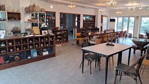 Een ruime woonkamer met een eettafel, meerdere stoelen en een keukenhoek met planken vol keramiek en keukengerei.