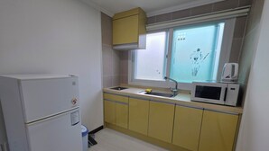 Een kleine keuken met een koelkast, magnetron, spoelbak en gele kastjes.