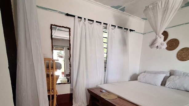 A bedroom with a bed, a bench, a mirror, and a window with curtains.