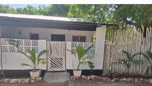 A house with a white exterior, a metal roof, and a gated entrance. There are two potted plants in front of the gate.