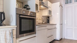 Moderni keittiö, jossa on ruostumattomasta teräksestä valmistetut kodinkoneet, valkoiset kaapit ja laatoitettu välitila.