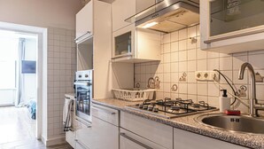 Moderni keittiö, jossa on valkoiset kaapit, kaasuliesi, ruostumattomasta teräksestä valmistettu pesuallas ja ikkuna pesualtaan yläpuolella.