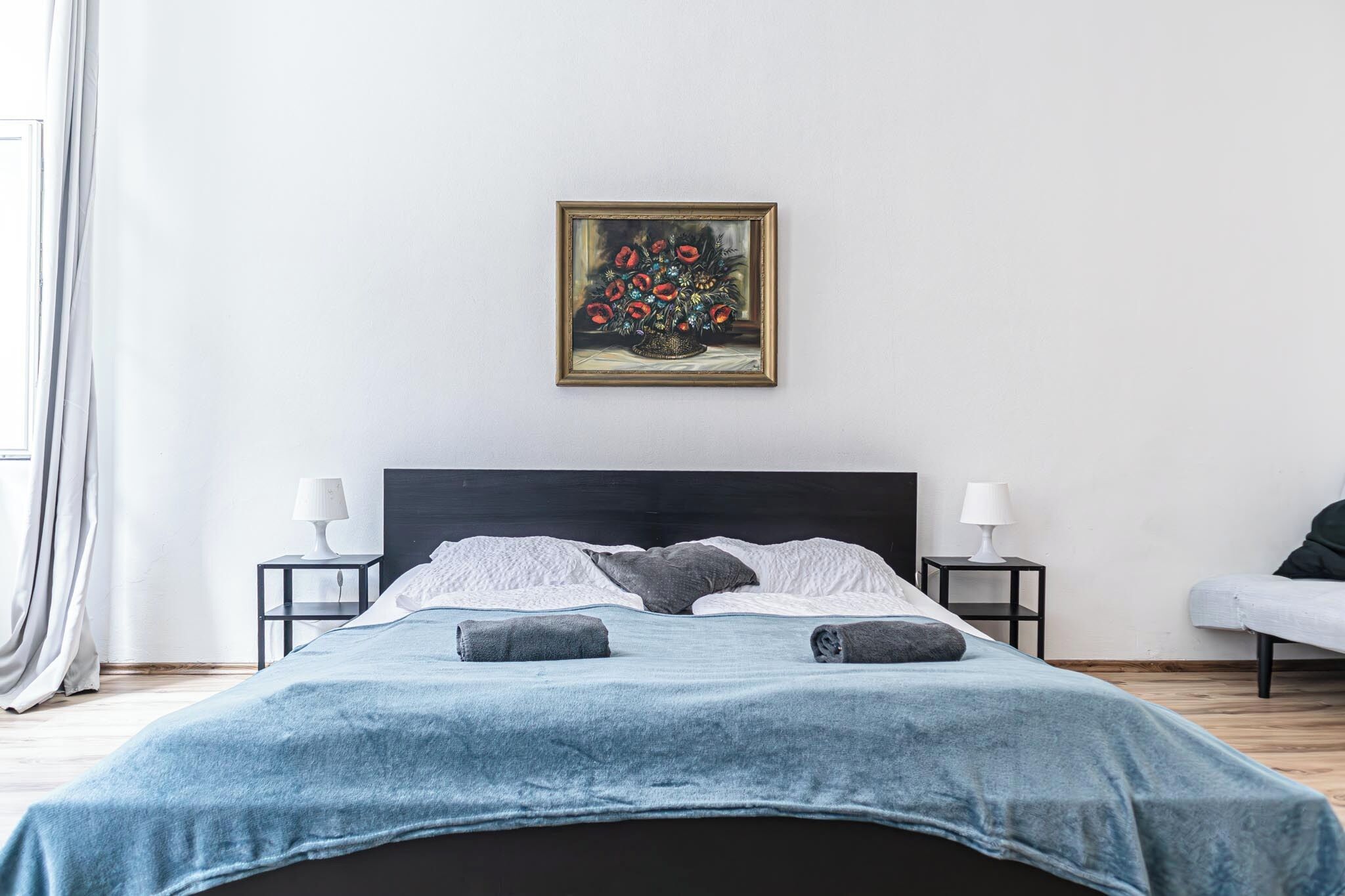 Quarto com uma cama, duas mesas de cabeceira com abajures, um quadro sobre a cama e uma janela com cortinas.