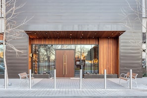 A modern building entrance with a large wooden door, glass windows, and a bench outside. - 2 Luxury Condos, 1 Block from Rainey St | New High Rise w/ Rooftop Pool & Gym (Austin)