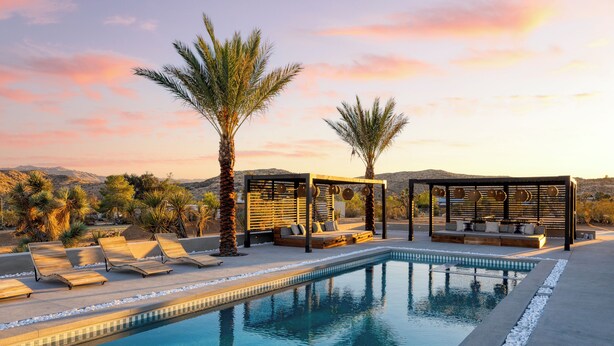 A pool area with lounge chairs, a seating area, and palm trees.