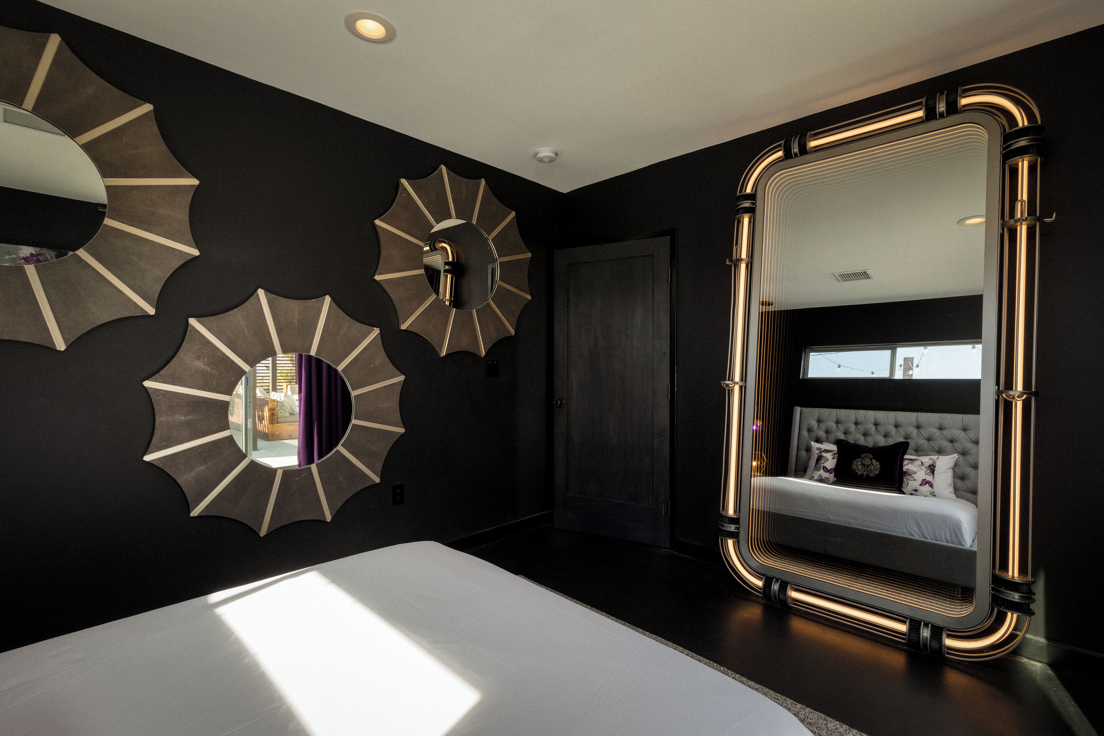 Un dormitorio moderno con una cama grande, un espejo con marco dorado y apliques decorativos en la pared.