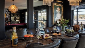A dining table set with wine glasses, cheese, and bread, in a room with a large window and a chandelier.