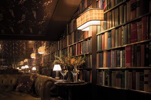 Eine Bibliothek mit Bücherregalen, einem Ledersofa und einem Tisch mit Lampe und Blumen.