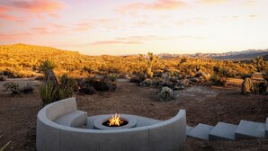 A desert landscape with a fire pit in the foreground and a mountainous backdrop.