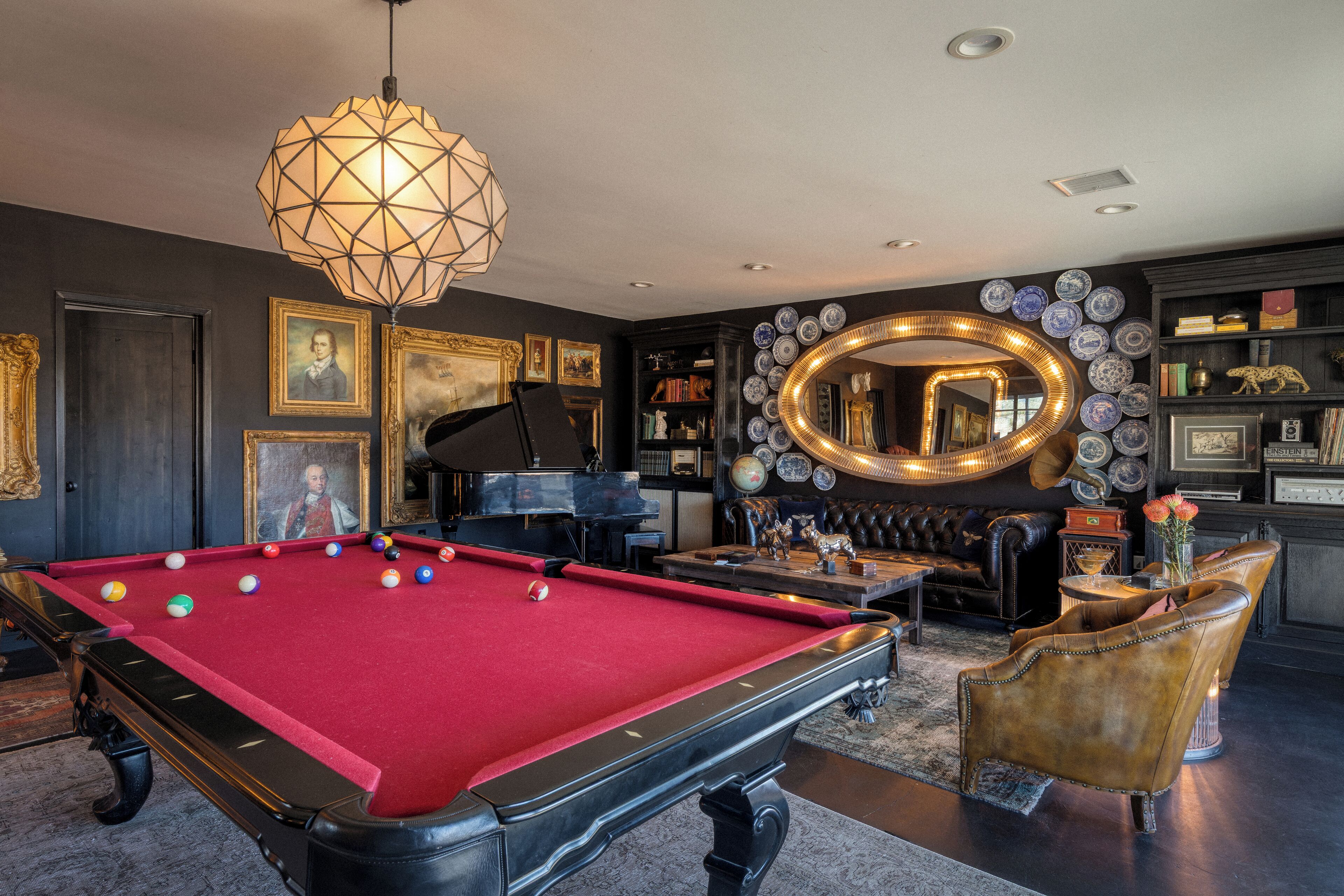 Une table de billard, un canapé en cuir, un miroir rond et une collection de tableaux encadrés.