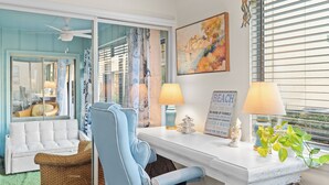 A room with a white sofa, a blue armchair, a white desk with two lamps, a potted plant, and a painting on the wall. - Steps from the Sand | Bright Coastal Stay w/ Pool Access | Coastal Hideaway (Destin)