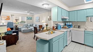 A modern kitchen with teal cabinets, a central island, and a dining area with a glass table. - Steps from the Sand | Bright Coastal Stay w/ Pool Access | Coastal Hideaway (Destin)