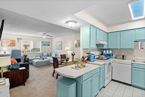 Une cuisine moderne avec des meubles de couleur turquoise, un îlot central et un coin repas doté d’une table en verre.