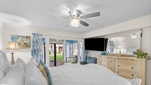 A bedroom with a large bed, a ceiling fan, a dresser, a TV, and a view of the outside. - Steps from the Sand | Bright Coastal Stay w/ Pool Access | Coastal Hideaway (Destin)