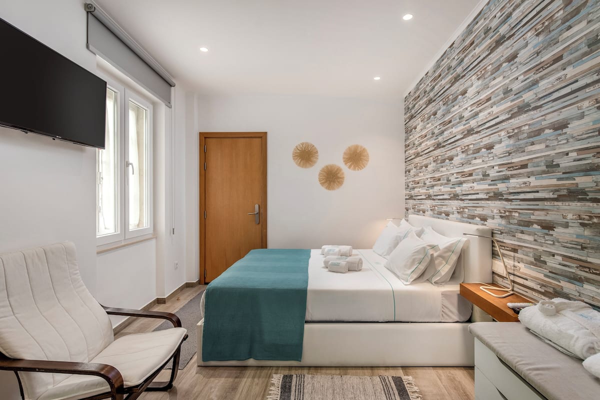 Una habitación de hotel moderna con cama, sillón, televisor de pantalla plana y una pared con un diseño de mosaico único.