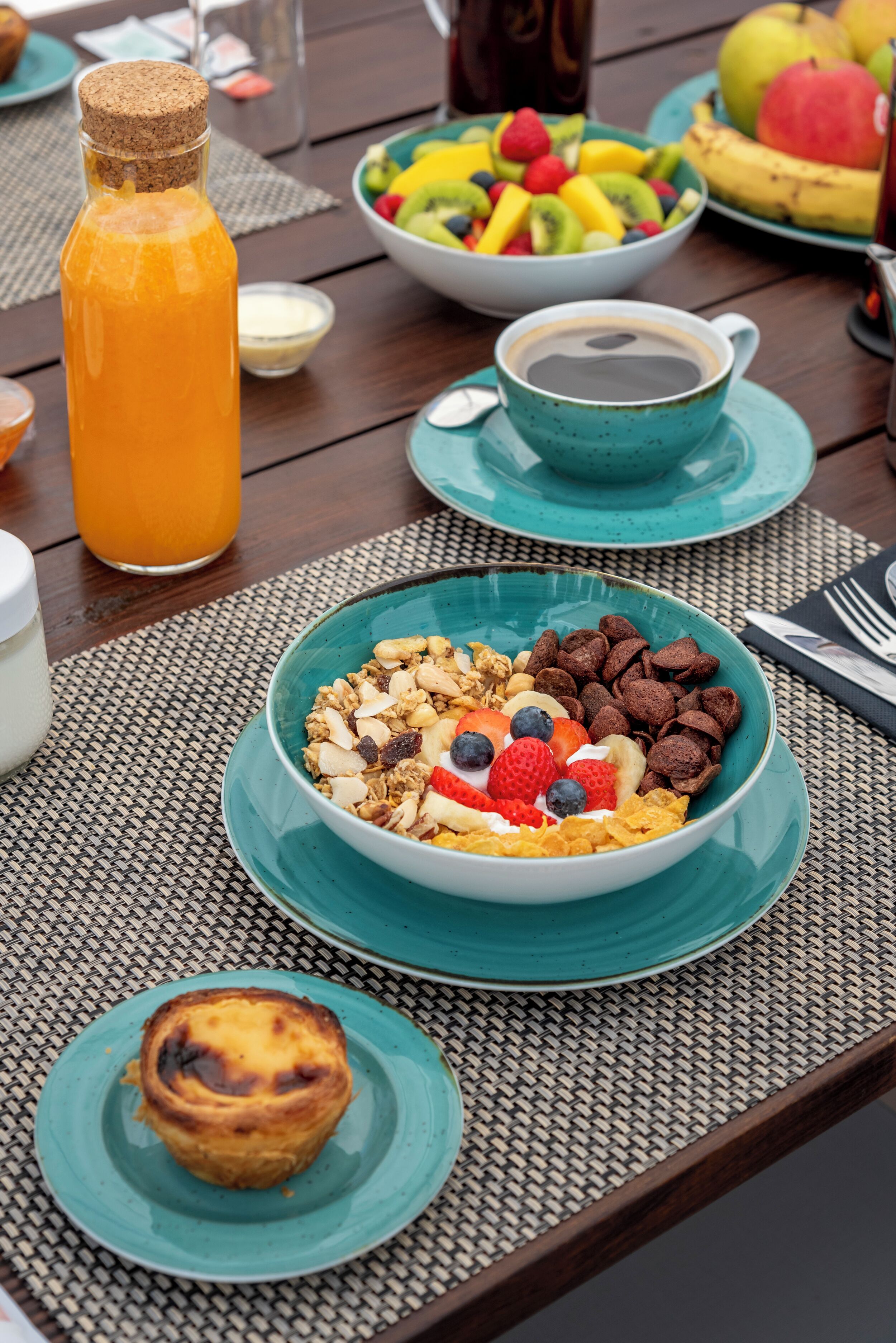 A breakfast table with a bowl of cereal, a cup of coffee, a bottle of orange juice, and a plate of fruit.