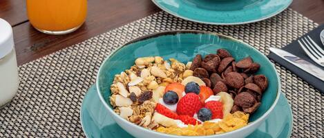 A breakfast table with a bowl of cereal, a cup of coffee, a bottle of orange juice, and a plate of fruit.