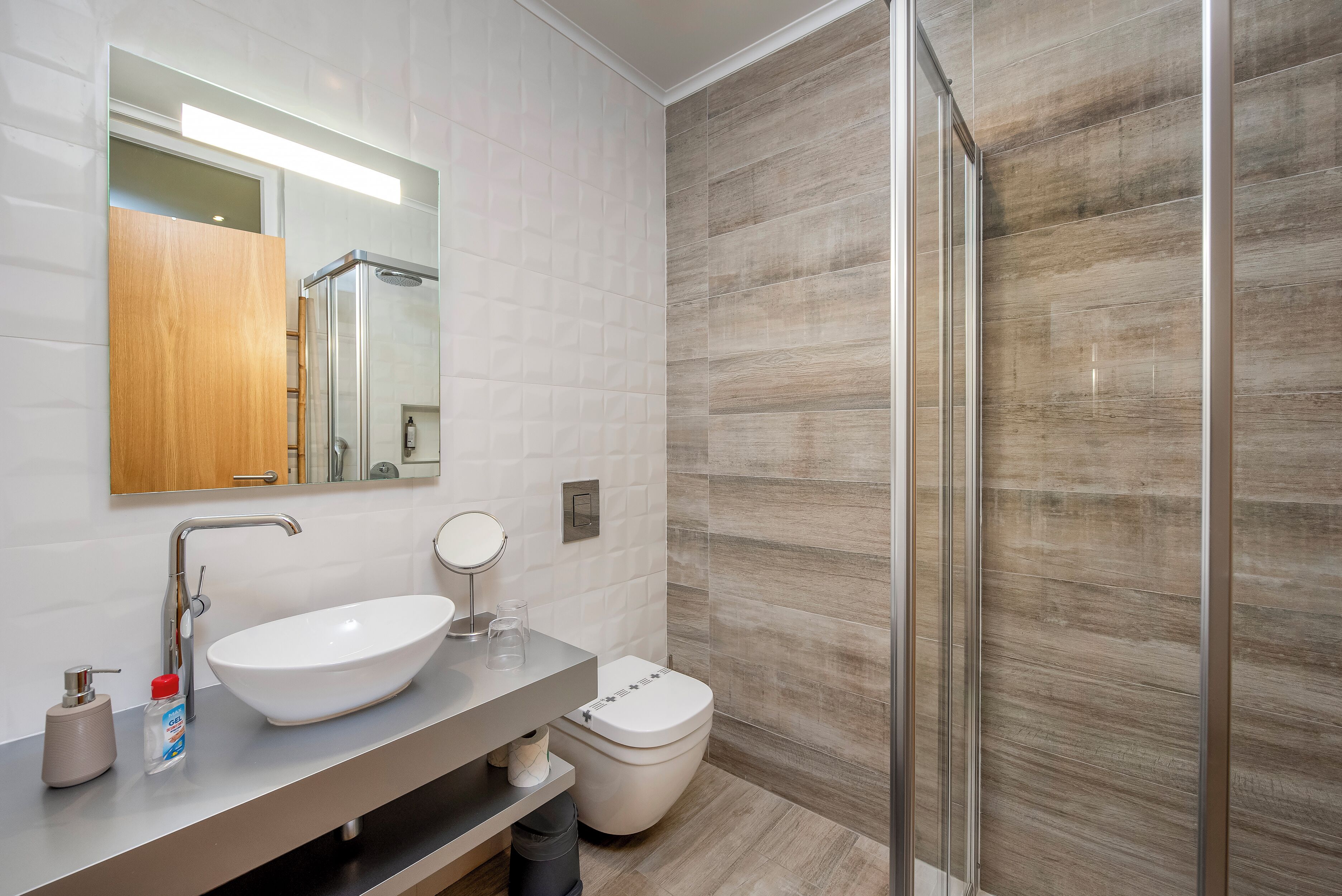 Ein modernes Badezimmer mit einem großen, weißen Waschbecken, einem Spiegel, einer Toilette und einer Duschkabine aus Glas.
