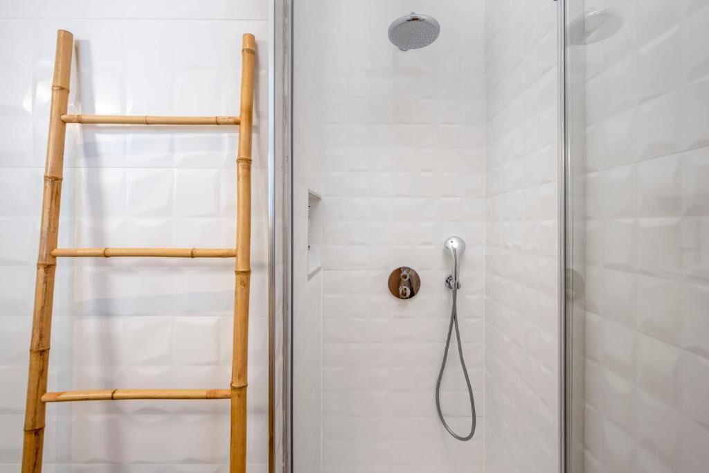 A glass-enclosed shower with a bamboo ladder, a handheld showerhead, and a wall-mounted control panel.