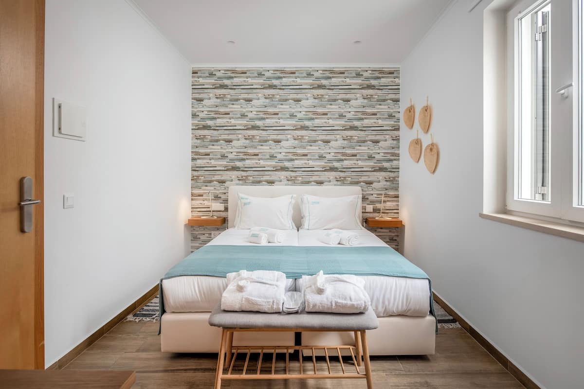 Un dormitorio ordenado con cama, un banco y una ventana.