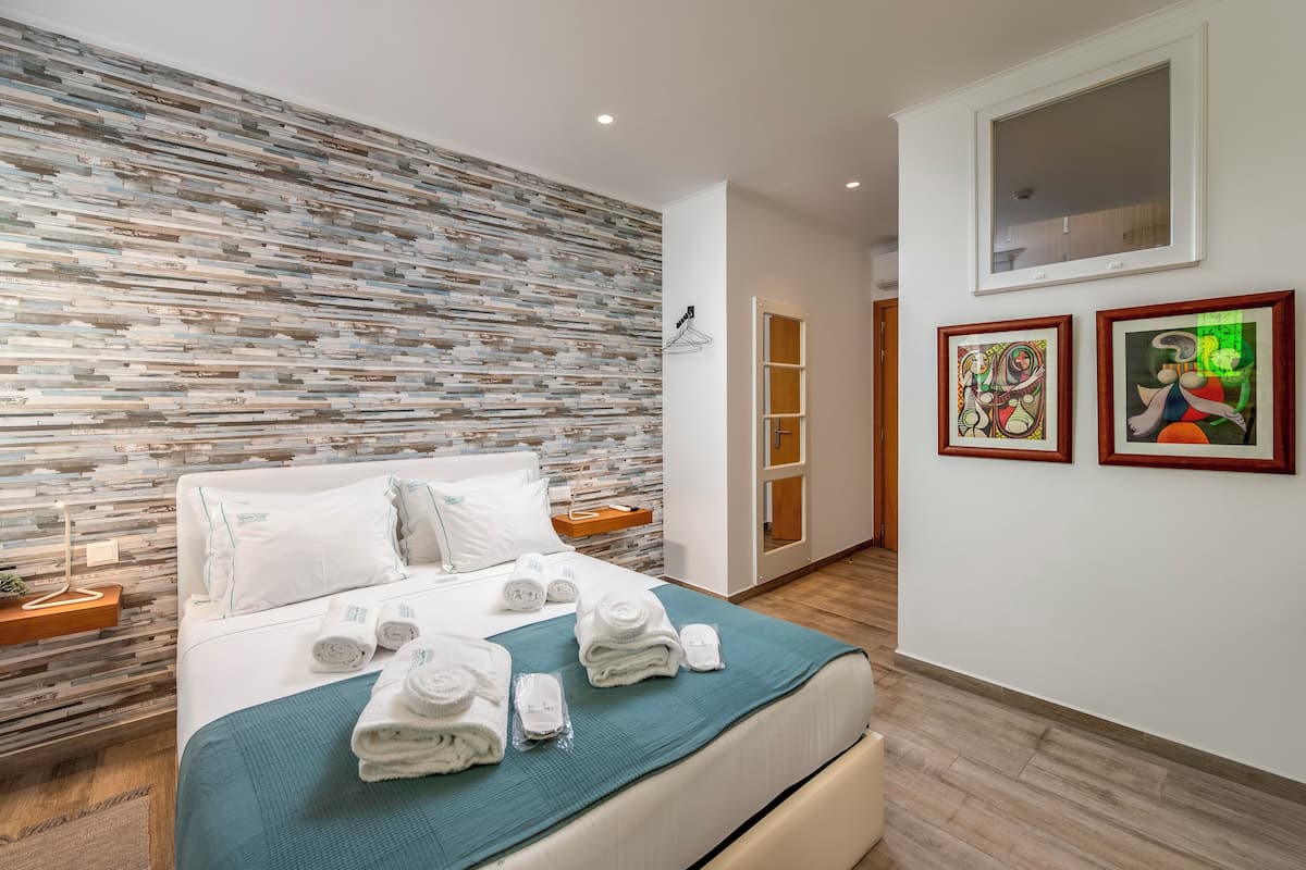 Una habitación de hotel moderna con una pared texturizada, una cama bien tendida con toallas, una mesita de noche y una obra de arte en la pared.
