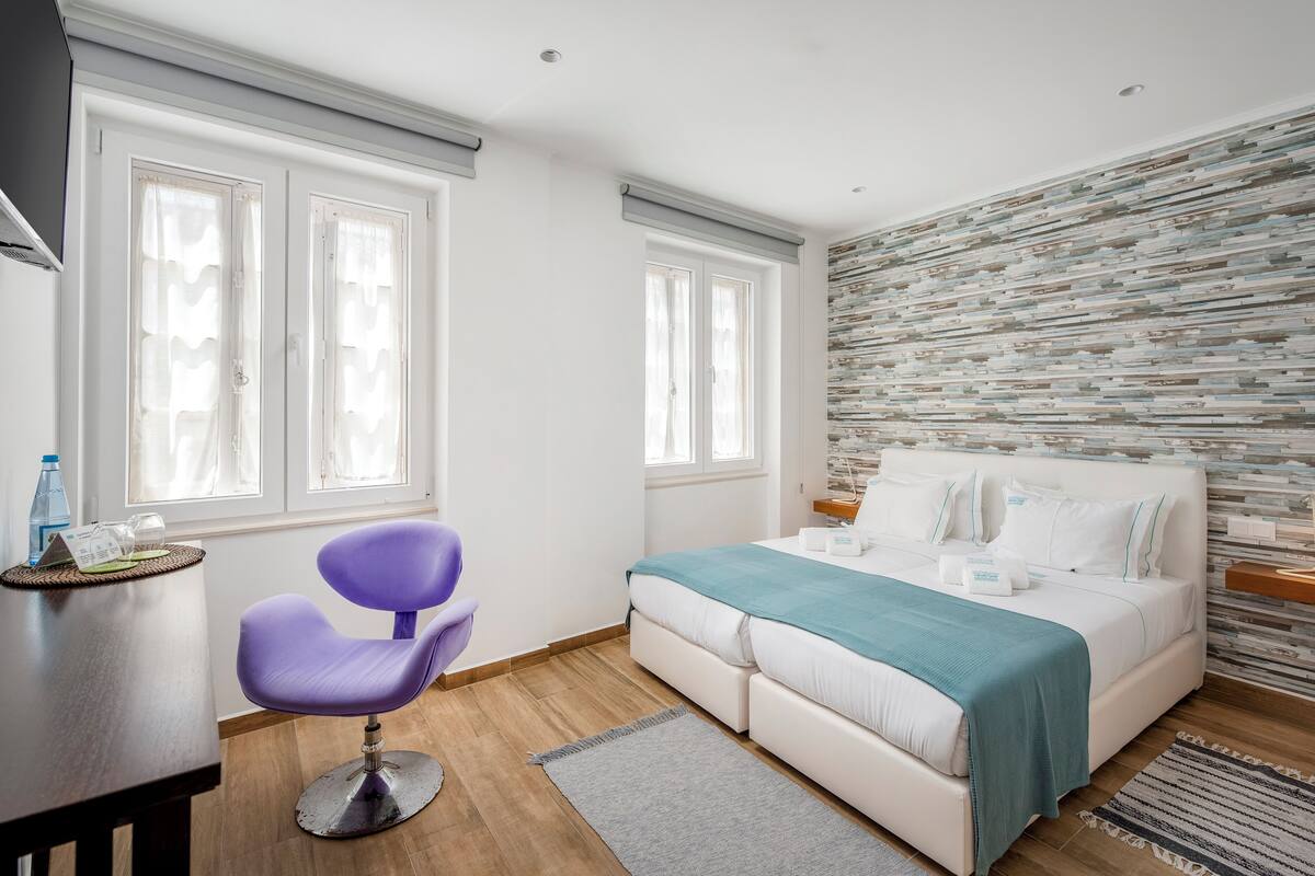 Un dormitorio moderno con una cama blanca, una silla morada y una pared con textura.