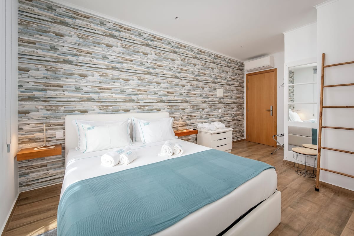 Una habitación de hotel moderna con una cama grande, suelo de madera, pared con diseño de piedra y una puerta de madera.
