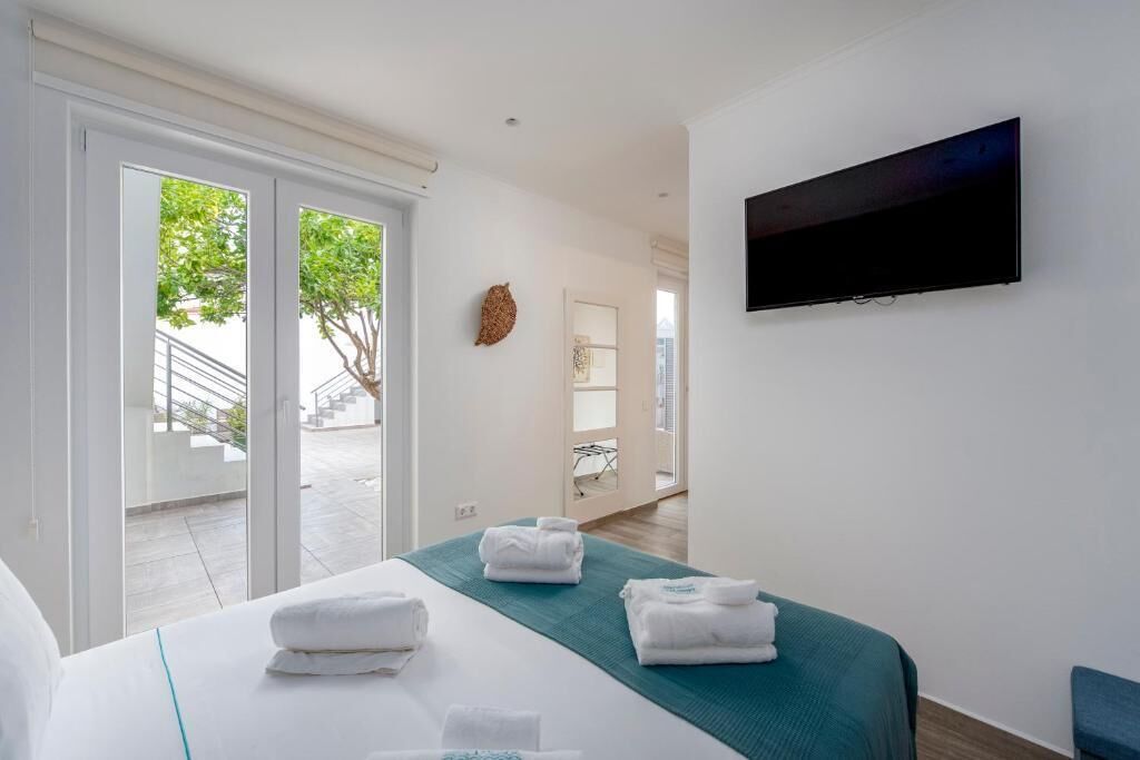 A hotel room with a bed, a TV mounted on the wall, and a view of the outside through the door.