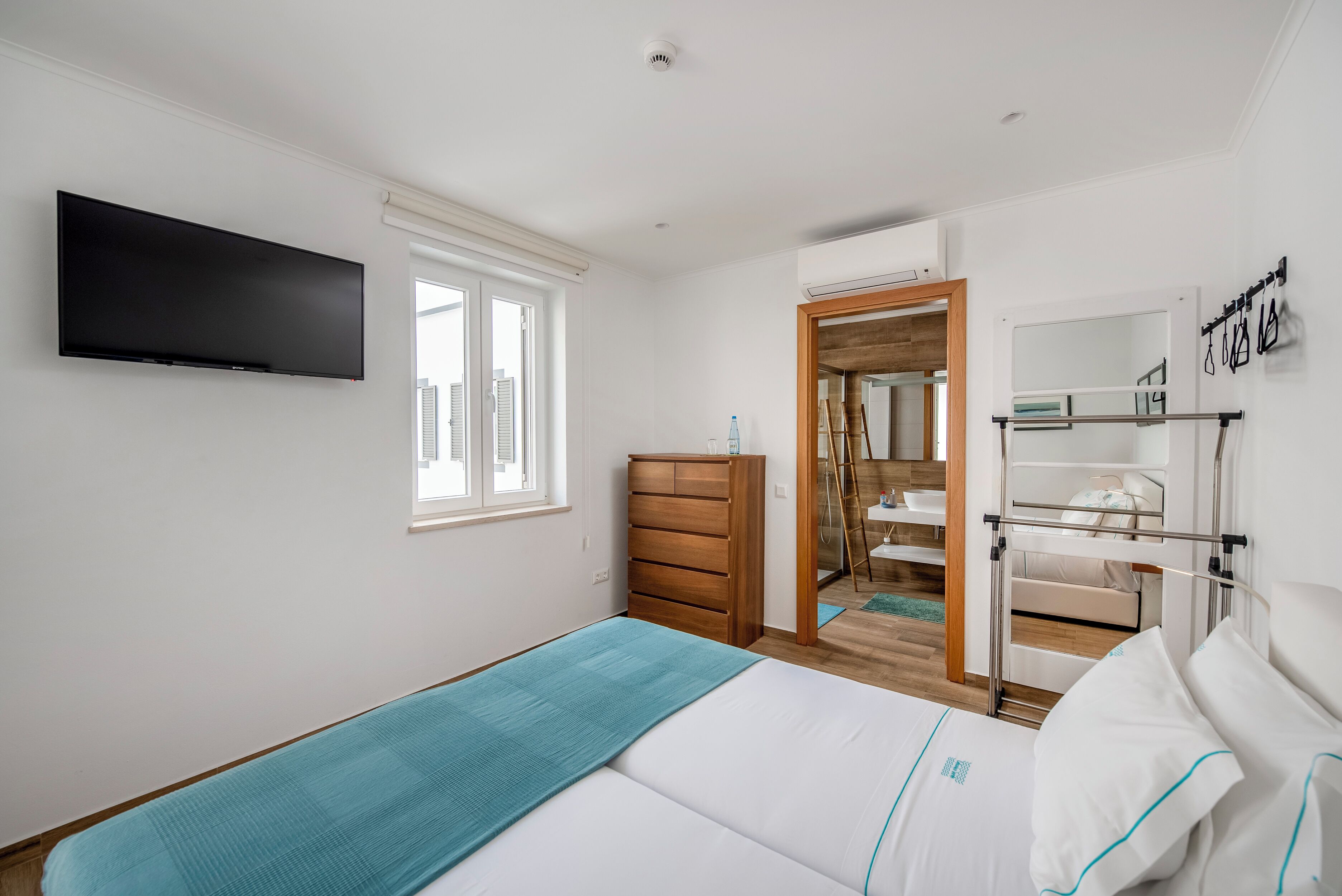 Un dormitorio con cama, cómoda, televisor y baño visible a través de una puerta abierta.