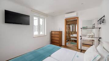 Un dormitorio con cama, cómoda, televisor y baño visible a través de una puerta abierta.