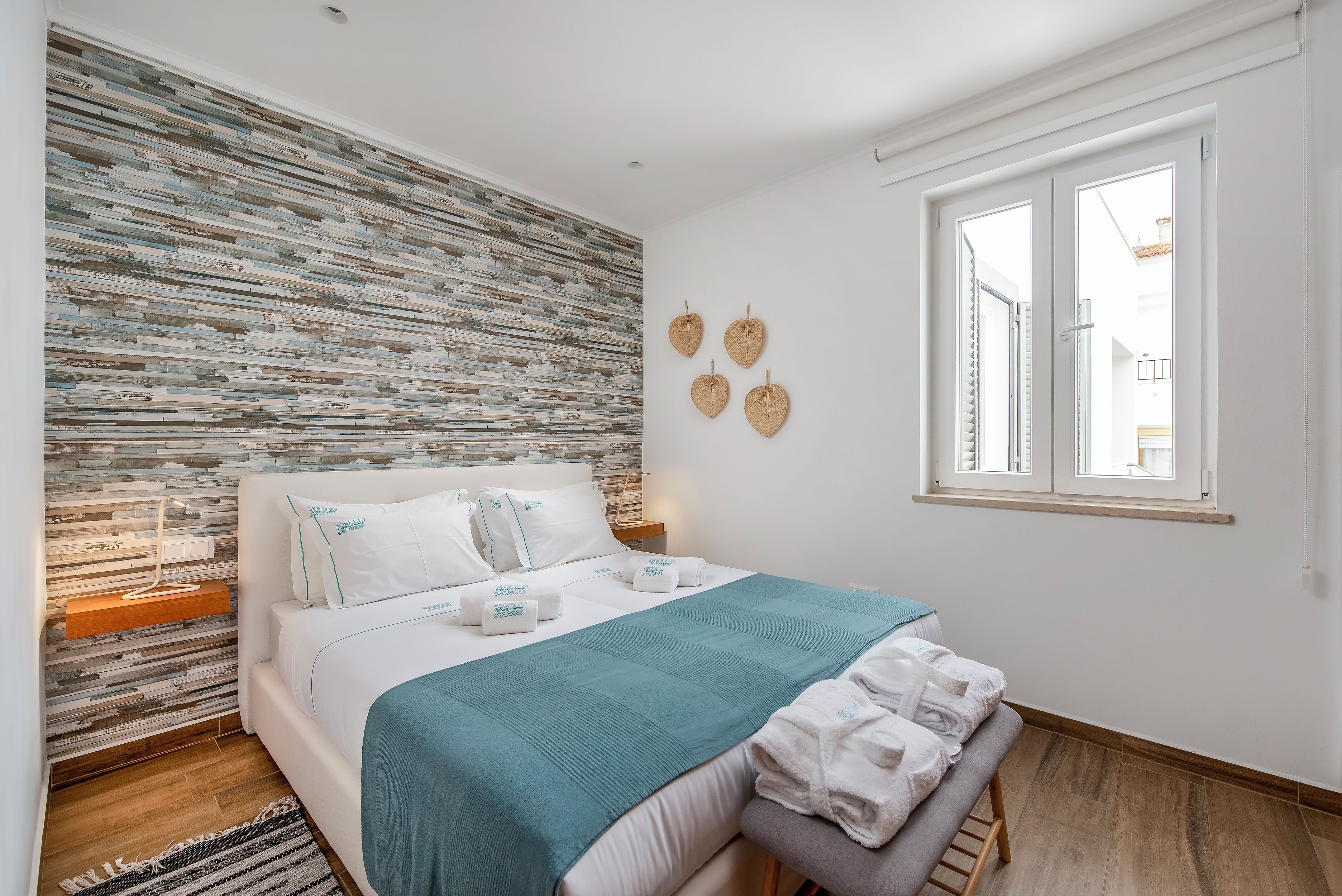 Un dormitorio ordenado con cama, mesitas de noche, una ventana y una pared con textura.