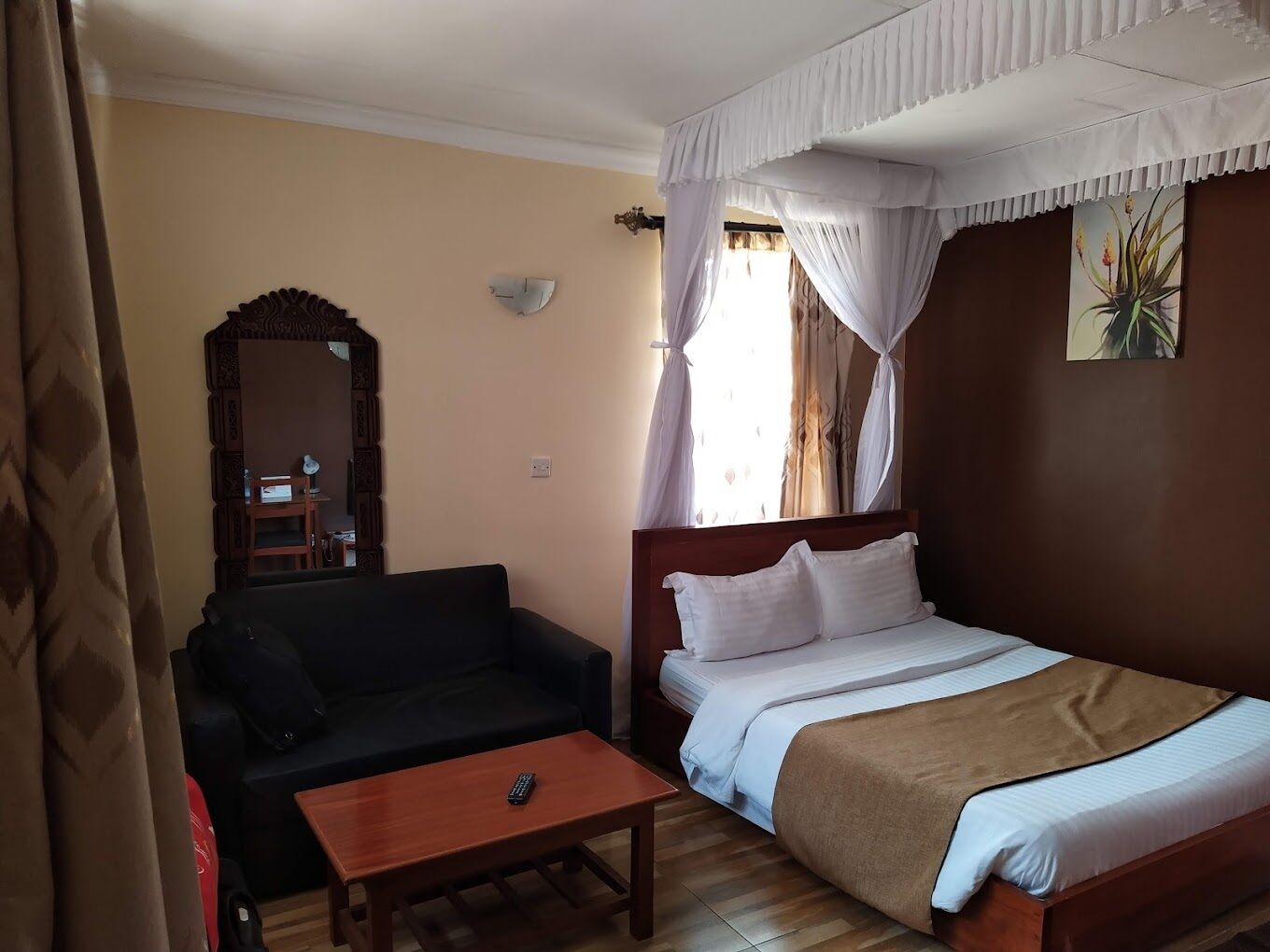 Une chambre d’hôtel avec un lit, un canapé, une petite table, un miroir et une fenêtre avec des rideaux.
