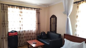Quarto de hotel com uma cama, uma mesa de madeira, um sofá preto e um espelho grande.